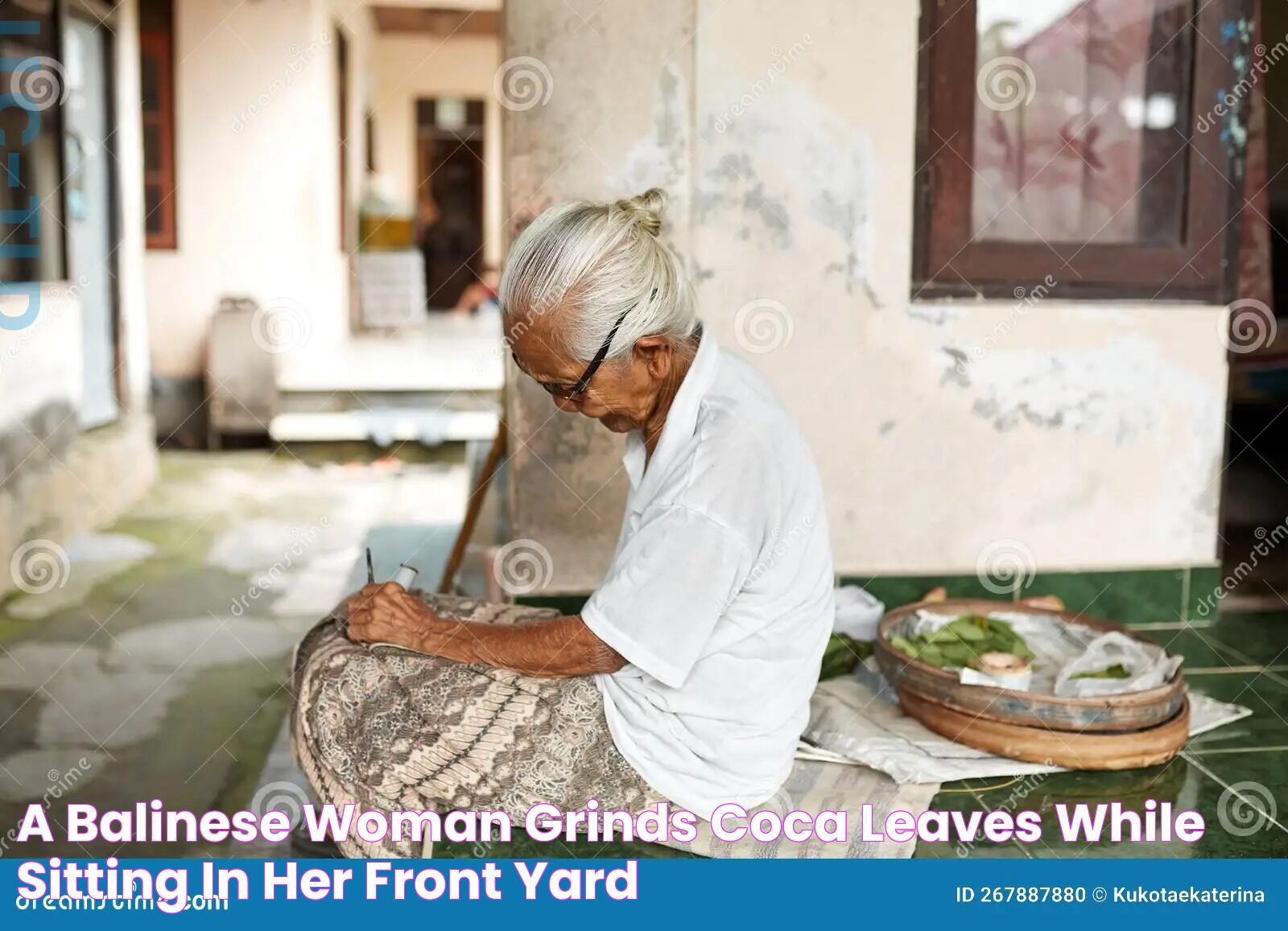 A Balinese Woman Grinds Coca Leaves while Sitting in Her Front Yard